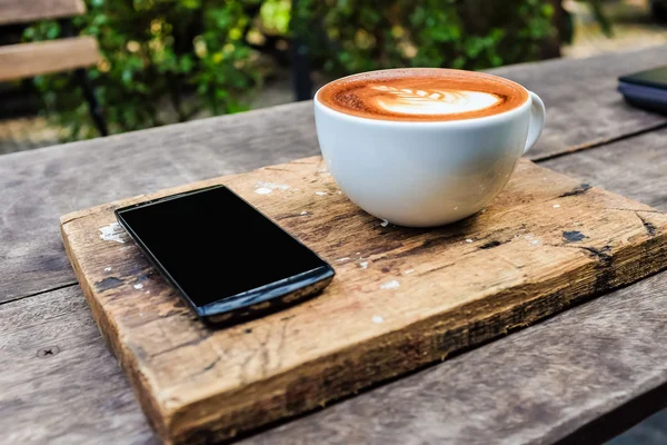 Smartphone with cup of latte art milk coffee leave texture on wo — Stock Photo, Image