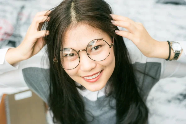 Beautiful asian young curly woman with glasses sitting on the bed — Stock Photo, Image