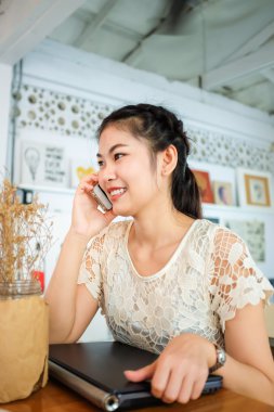 Asyalı güzel kız cep telefonu kafede konuşuyor. Bir kafede akıllı telefon kullanan kadın.