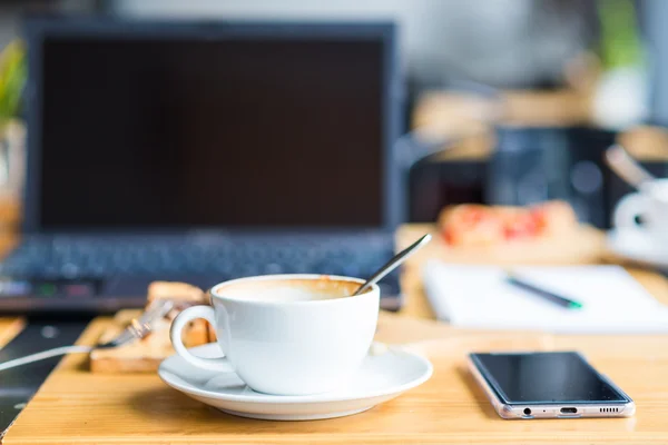 Laptop with cup of coffee and telephone on old wooden table. — Stock Photo, Image