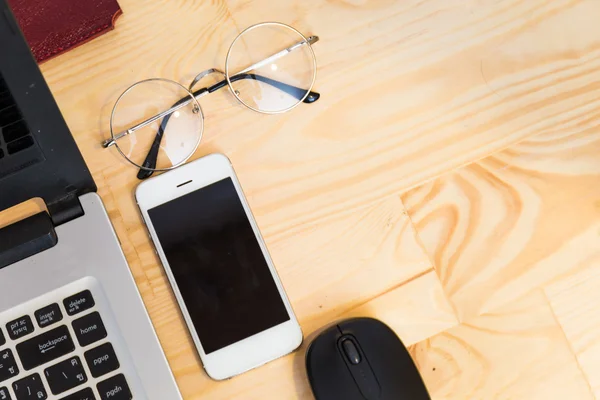 Ноутбук со смартфоном и очками на деревянном столе — стоковое фото