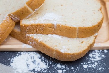 Kepekli ekmek ahşap plaka siyah arka plan üzerine bıçakla dilimlenmiş.