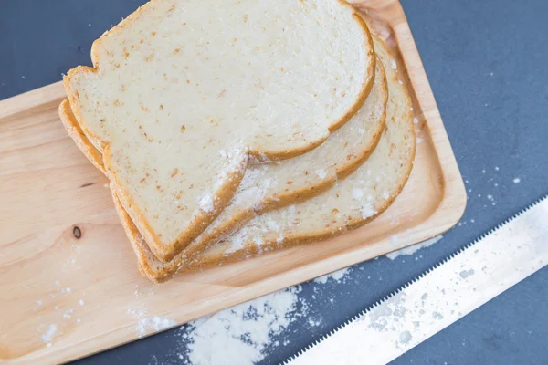 Pão de trigo integral fatiado em placa de madeira fundo preto — Fotografia de Stock