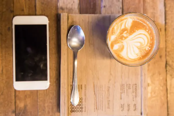 Puchar lattecoffee na drewnianym stole z smartphone — Zdjęcie stockowe