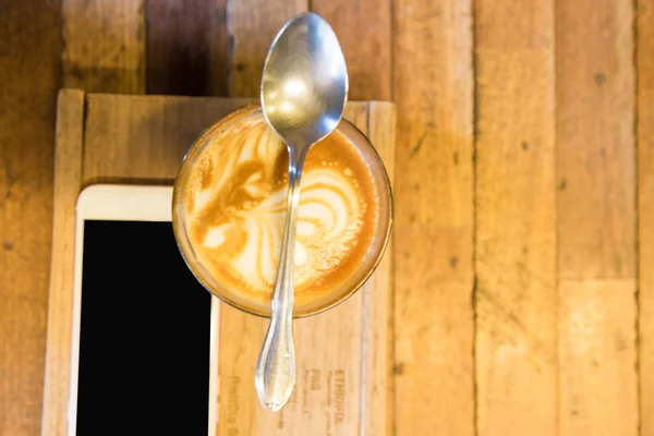 Xícara de lattecoffee em uma mesa de madeira com smartphone — Fotografia de Stock