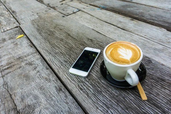Latte coffee cup and cellphone for business on wood table, Selective focus on coffee.
