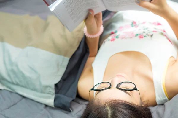 Окуляри жінка лежить в ліжку, читаючи книгу — стокове фото