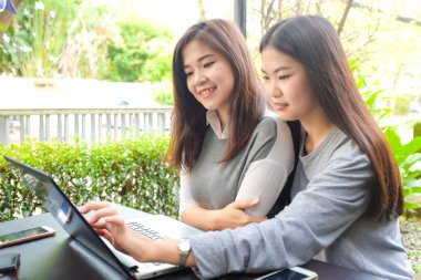 Mutlu iki Asyalı kadın dizüstü bilgisayar ve park açık otururken konuşurken iş kullanma