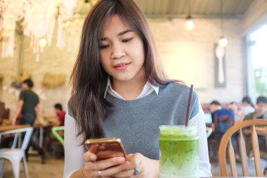 Güzel Asyalı genç kadın iş konuşurken rahat sanat kahve dükkanında otururken cep telefonu kullanarak