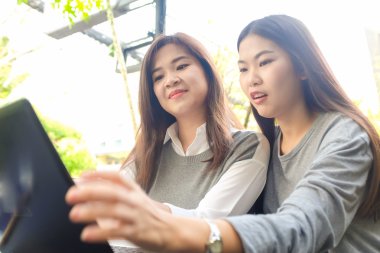Mutlu iki Asyalı kadın dizüstü bilgisayar ve park açık otururken konuşurken iş kullanma