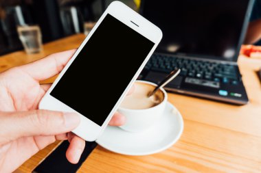 Kahve dükkanındaki tatlı ve laptop ile Smartphone kullanarak ele