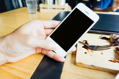 Kahve dükkanındaki tatlı ve laptop ile Smartphone kullanarak ele