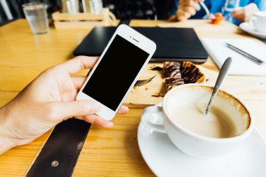 Kahve dükkanındaki tatlı ve laptop ile Smartphone kullanarak ele