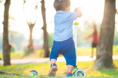 Şehir parkında çimenlerde motosiklet süren sevimli Asyalı çocuk gün batımında egzersiz yapıyor.