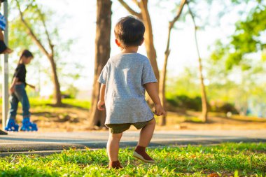 Asyalı çocuk yeşil çimlerde yürüyor. Şehir parkında gün batımını seyrediyor. 1-2 yaşında bir çocuk.
