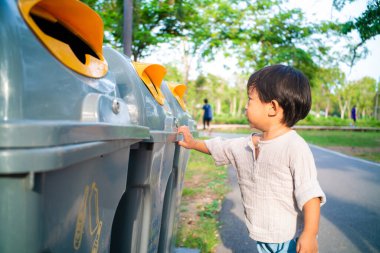 Şehir parkındaki geri dönüşüm kutusuna plastik şişe atan küçük çocuk çevre kavramını korumak için...