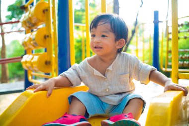 Küçük Asyalı çocuk oyun parkında plastiği kaydıran çocuğu oynuyor yeşil ağaç arka planında. Egzersiz konsepti öğreniliyor.