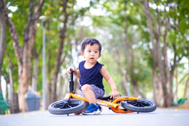 Şehir parkında bisiklet süren sevimli genç çocuk asfalt yolda bulanık yeşil ağaç arka planda