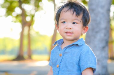 Şehir parkında gülümseyen Asyalı çocuk. Arka planda bulanık ağaç. Gün batımı ışığı.