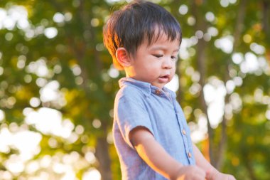 Şehir parkında gülümseyen Asyalı çocuk. Arka planda bulanık ağaç. Gün batımı ışığı.