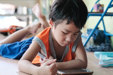 Akıllı telefondan oyun oynayan Asyalı çocuk evde oturmuş internet oyunu oynuyor.