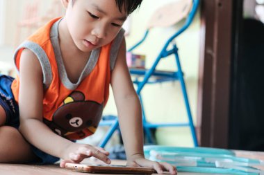 Akıllı telefondan oyun oynayan Asyalı çocuk evde oturmuş internet oyunu oynuyor.