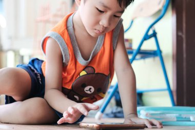 Akıllı telefondan oyun oynayan Asyalı çocuk evde oturmuş internet oyunu oynuyor.