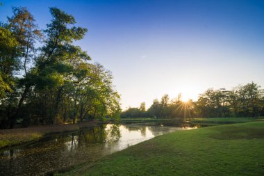 Göletin doğal arka planına sahip yeşil parkta gün batımı