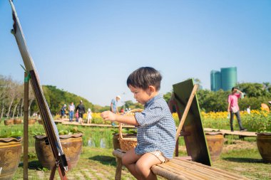 Çiçek parkında kağıda resim çizen Asyalı çocuk.