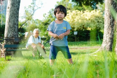 Doğada, parktaki yeşil çimlerde yürüyen sevimli Asyalı çocuk.