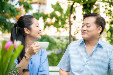 Bahçe parkında yemek ve içecek pikniği olan yaşlı çift birlikte bakım hakkında konuşuyorlar, Asyalı emekli çift.