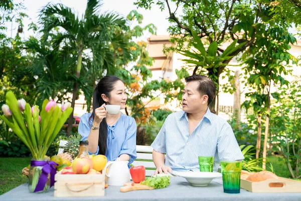 Senior couple with food and drink picnic in garden park talking care together, Asian retirement couple