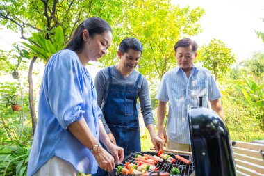 Park 'ta barbekü ızgara yemek partisi veren Asyalı mutlu bir arkadaş.