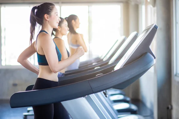 Attractive asian sport women running on treadmil with friend in sport gym healthy women