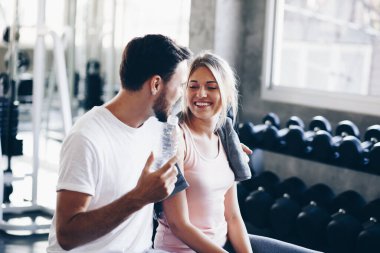 Spor salonundaki genç beyaz çift egzersizden sonra su içip sohbet ediyorlar. Sağlıklı aşk kavramı