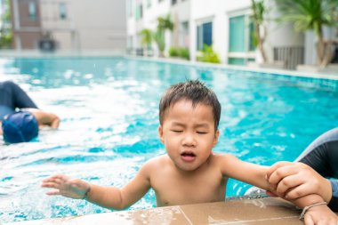Annesiyle yüzen küçük Asyalı çocuk modern apartman havuzunda yüzüyor.