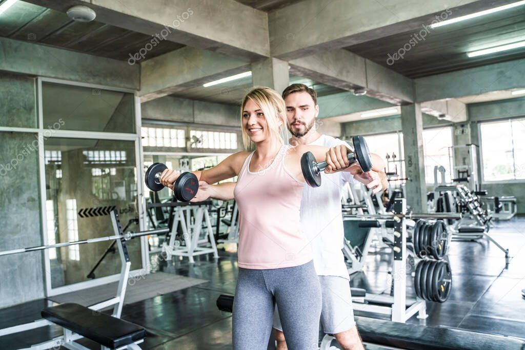 Woman with her personal fitness trainer lifting dumbells in fitness sport gym