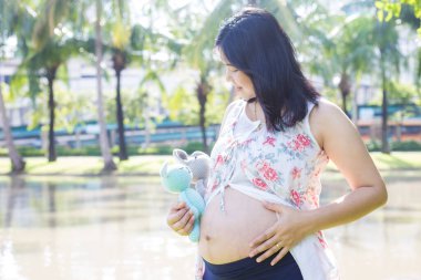 Asyalı genç, mutlu, hamile bir kadın doğa parkında rahatlıyor ve hayatın tadını çıkarıyor.