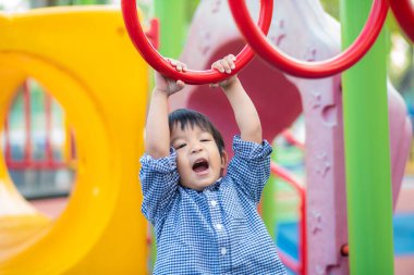 Mutlu Asyalı çocuk, anaokulu çocuğunun eğlence parkındaki çocuk parkının barına tırmanıyor.