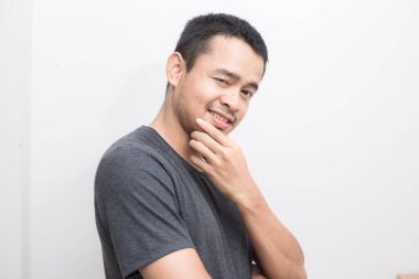 Beyaz arka planda, kısa kollu gri tişörtlü, gülümseyen zeki Asyalı genç adam.