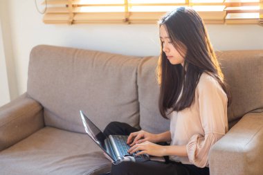 Genç Asyalı kadın rahat bir koltukta otururken bilgisayarla iş bağlantısı kuruyor.