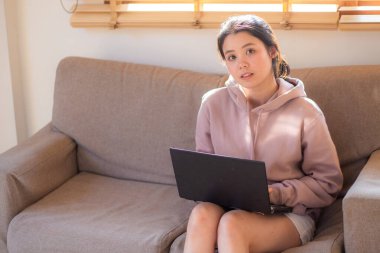 Genç Asyalı kadın rahat bir koltukta otururken bilgisayarla iş bağlantısı kuruyor.