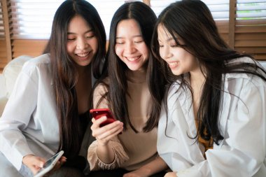 Ofisteki kanepede oturan akıllı telefon kullanan bir grup kız arkadaş.