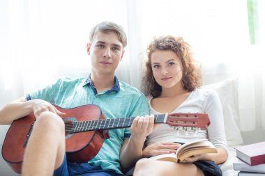 Aşk çifti beyaz odada gitarla eğleniyor Mutlu erkekler ve kadınlar