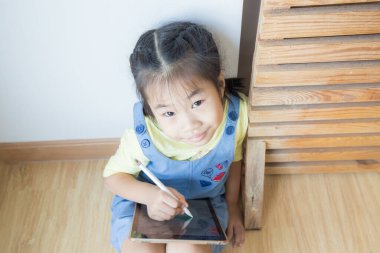 Anaokulu kızı tablet bilgisayar kullanıyor. Rahat bir odada online eğitim alıyor.