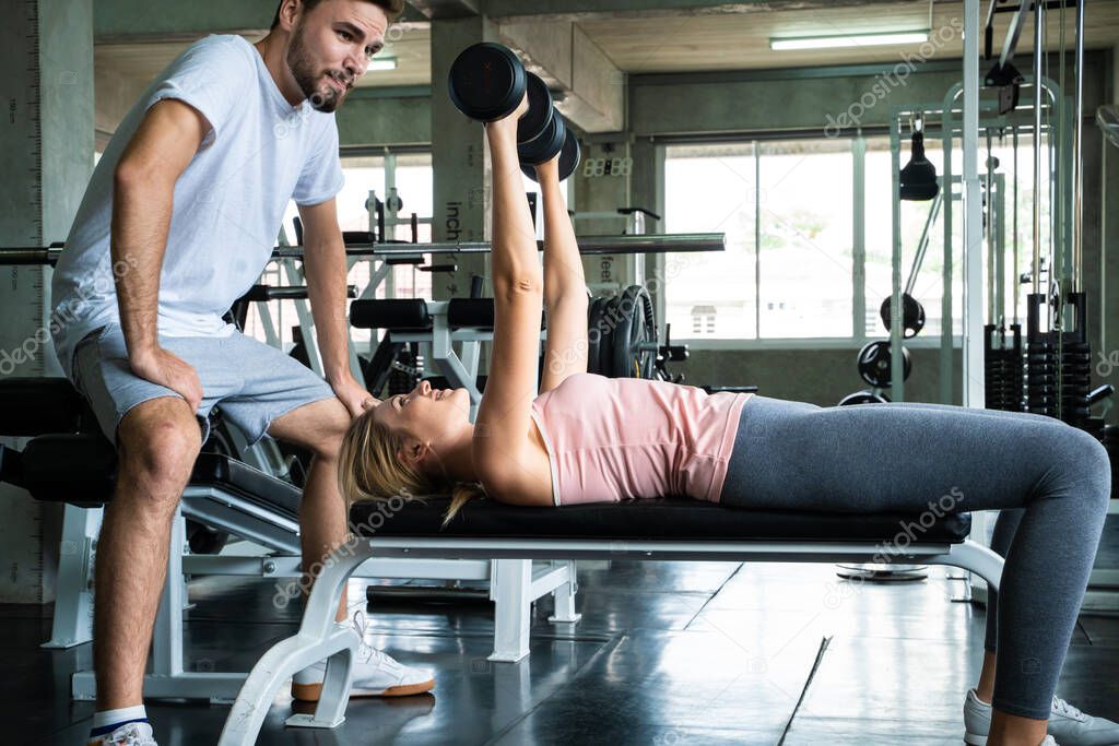 Woman with her personal fitness trainer lifting dumbell in fitness sport gym healthy activity