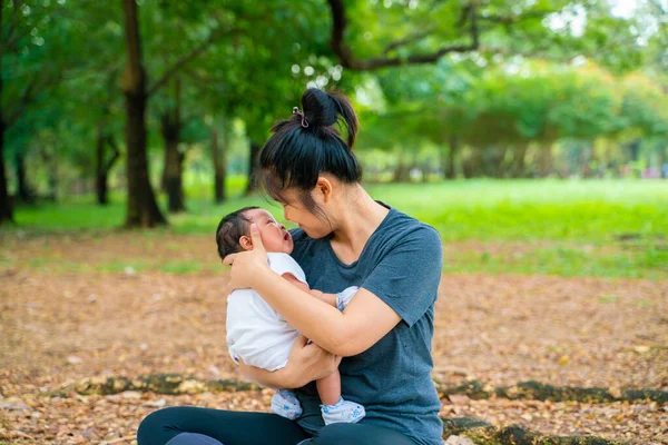 Mother hold carry infant baby boy sitting under tree branch morning relax nature