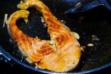 Kızarmış somon bifteği ve siyah tavada deniz ürünleri.