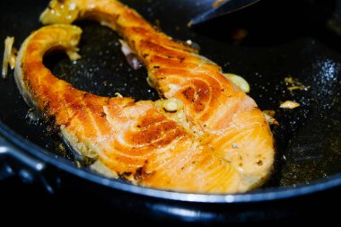 Kızarmış somon bifteği ve siyah tavada deniz ürünleri.