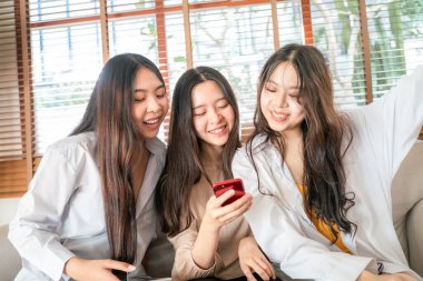 Ofisteki kanepede oturan akıllı telefon kullanan bir grup kız arkadaş.